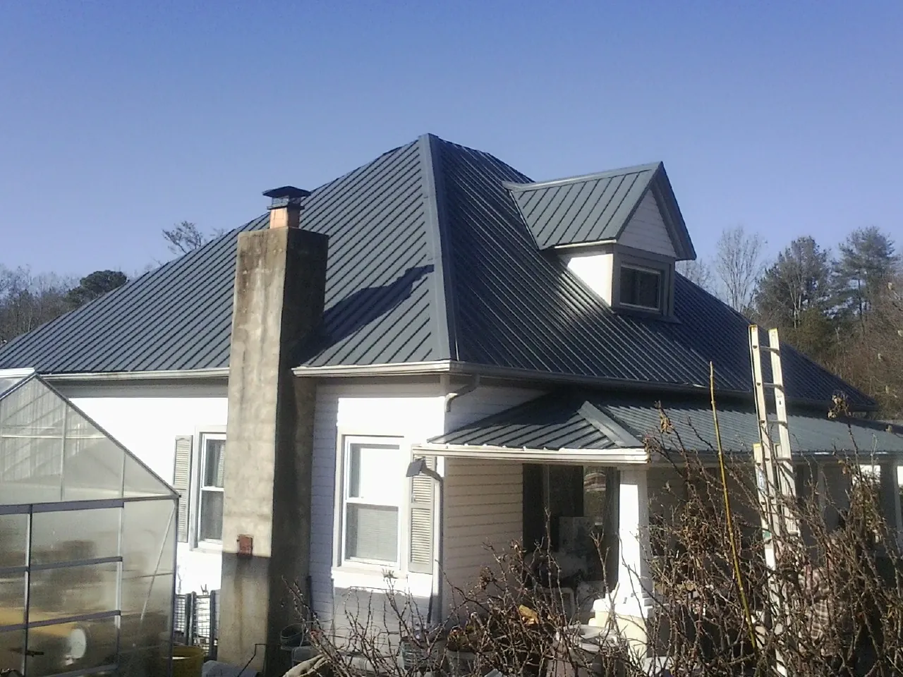 Dark blue standing seam metal roof on a white farmhouse with dormer — Slate & Tile Roof Repair by Roofing Brothers in Silsbee