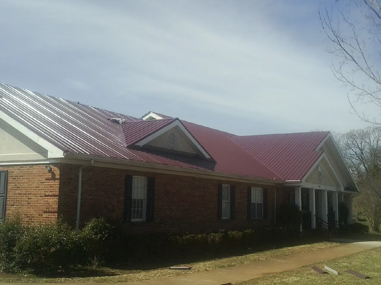 Red metal roof with gabled entries on a long brick building, from a Hail Damage Roof Repair job in Silsbee