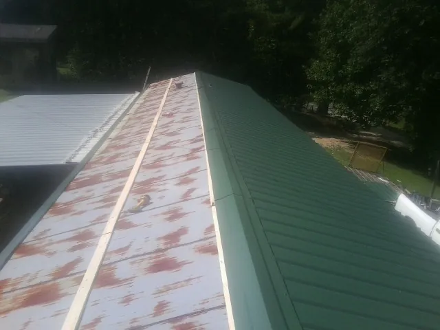 Old rusted panels beside newly installed green metal roofing — Wind Damage Roof Repair by Roofing Brothers in Silsbee
