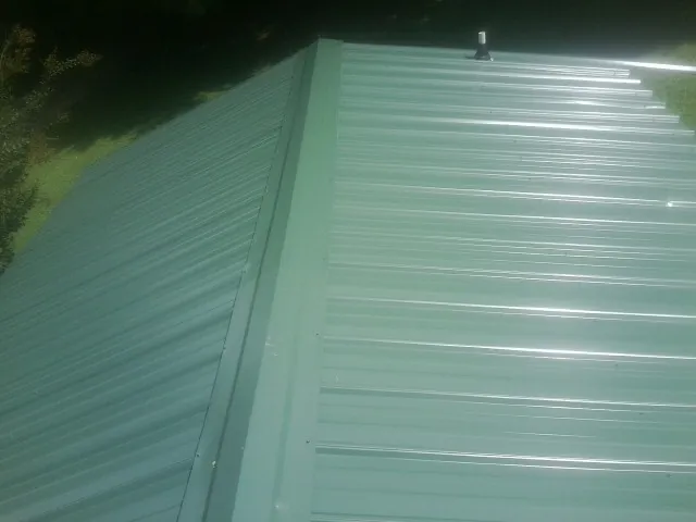 New green metal panels meeting at the ridge of a roof — Flat Roof Repair work by our crew in Silsbee