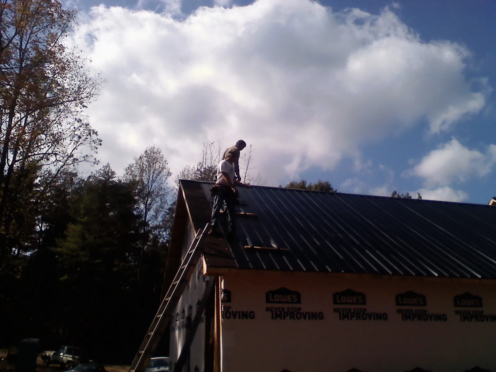 Roofer fastening dark metal panels high against a cloudy sky, from a Roof Inspection job in Silsbee
