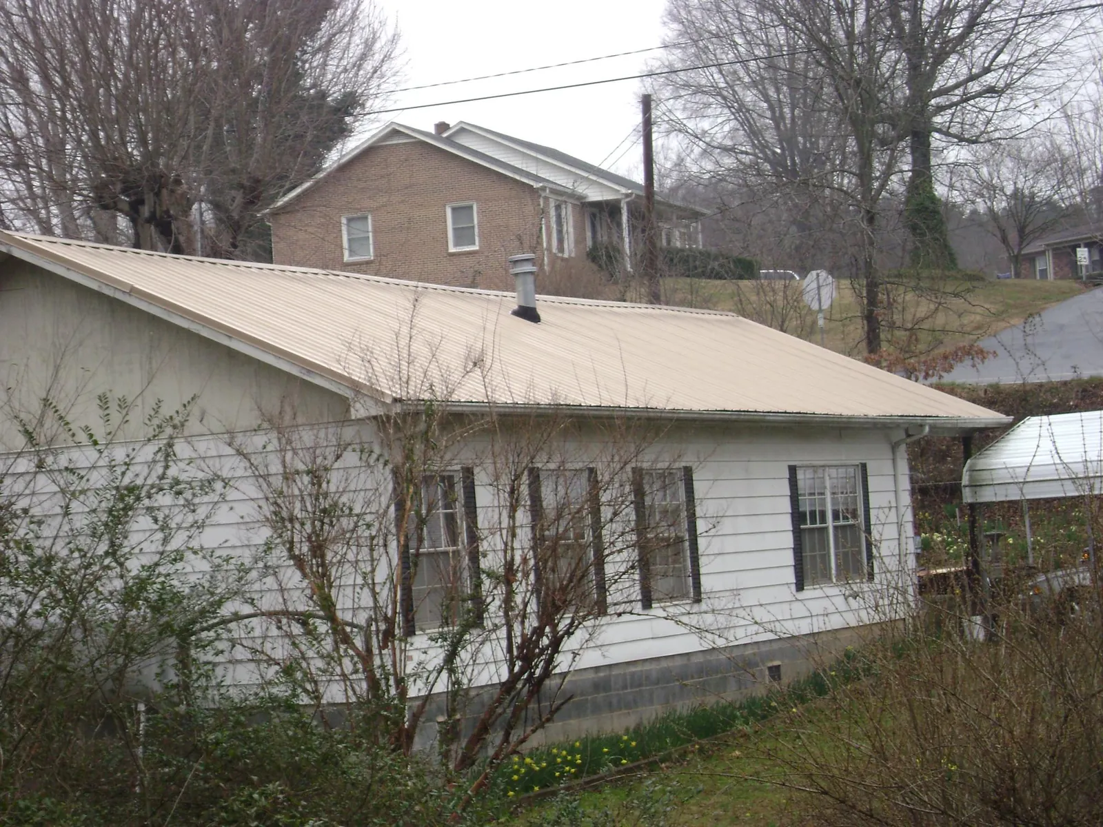 Tan metal roof on a white sided house set into a hillside — Commercial Roofing by Roofing Brothers in Silsbee