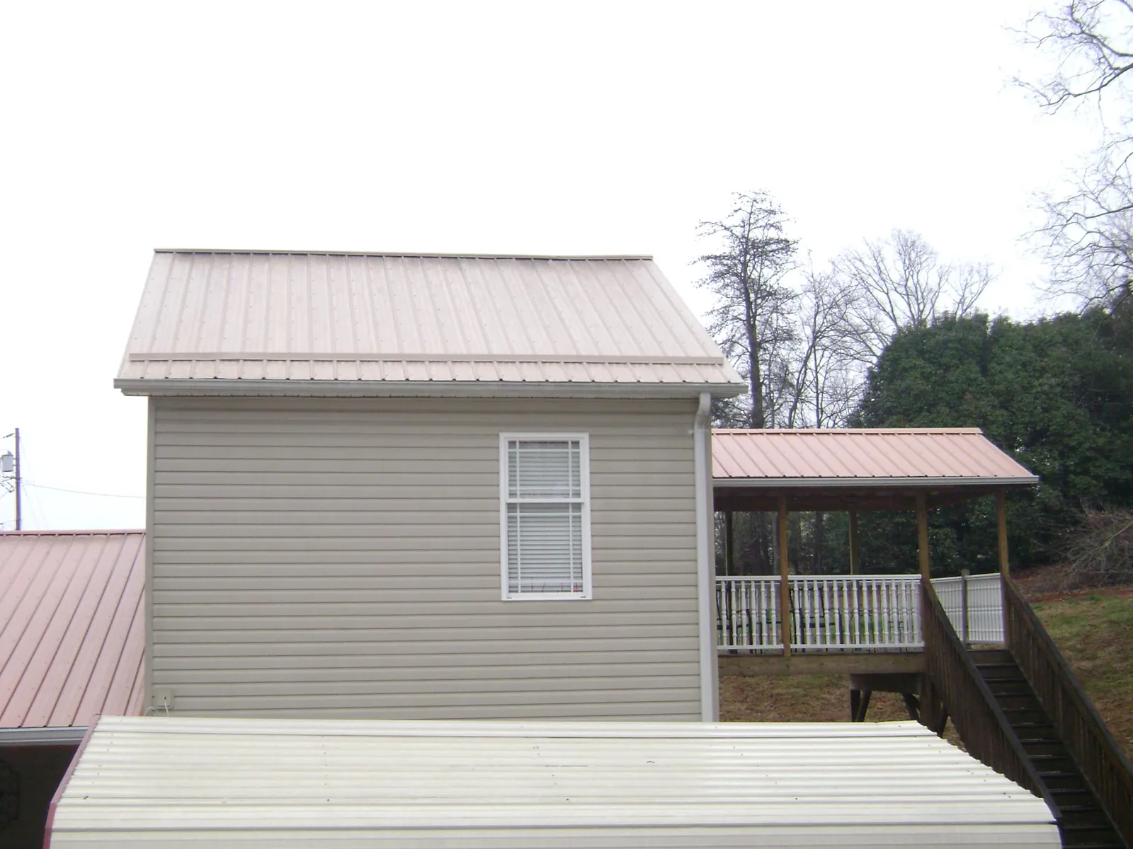 Tan metal roofs on a two story addition and attached porch, from a Roof Replacement job in Silsbee